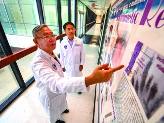 Two researchers wearing lab coats look at a research poster, with one pointing at it