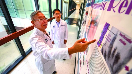Two researchers wearing lab coats look at a research poster, with one pointing at it