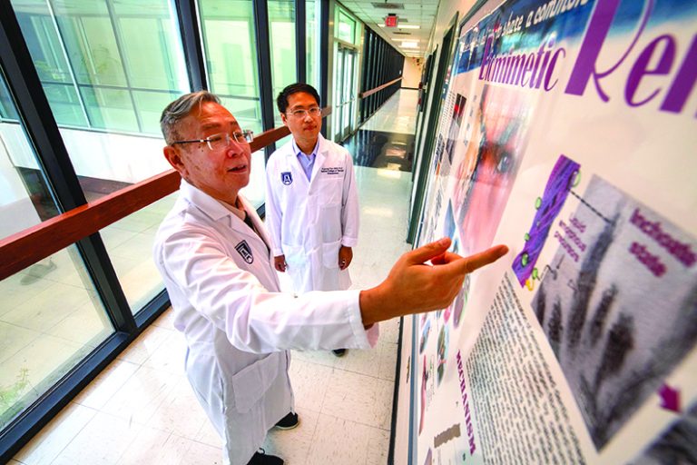 Two researchers wearing lab coats look at a research poster, with one pointing at it