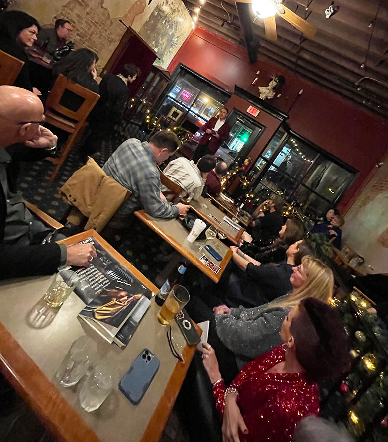 A man standing in front of a group of people in a room and speaking to them around Christmas time.