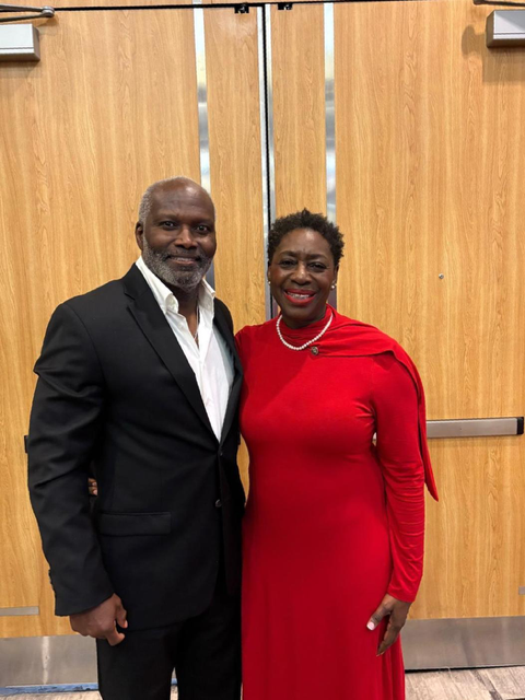 A woman and man pose together in front of wooden doors to a ballroom