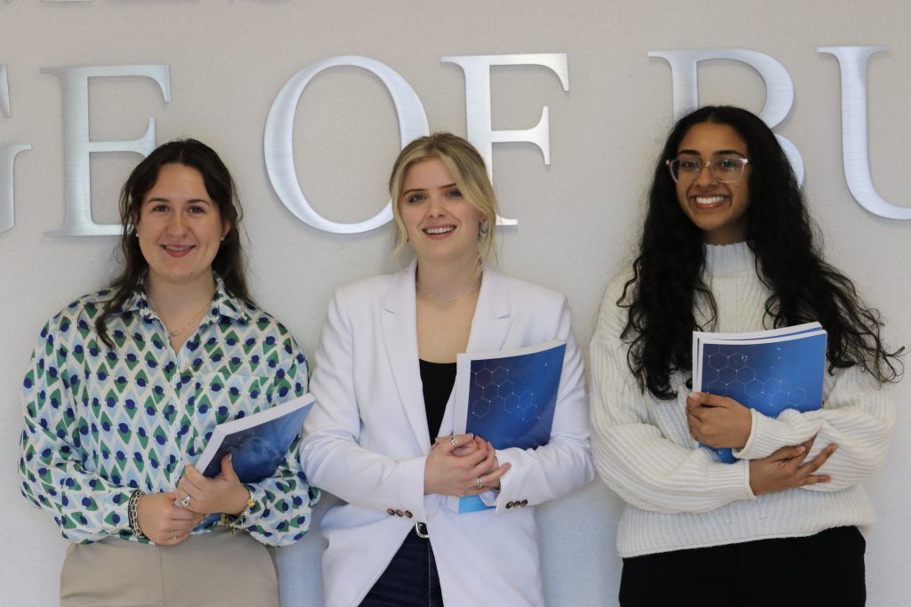 3 students posing and smiling holding books