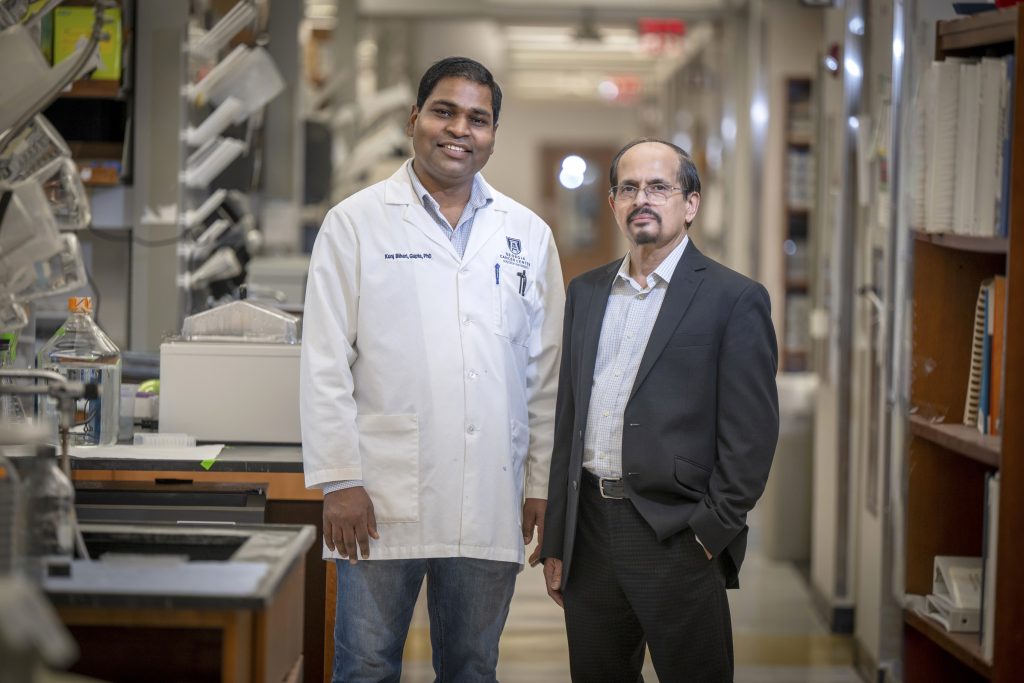 In this photo, you see two men standing next to one another. The man on the left is wearing a white lab coat. The photo was taken inside the Georgia Cancer Center's M. Bert Storey Research Building.