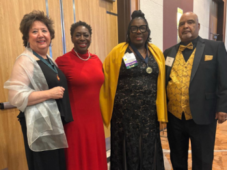 Four people stand together in evening attire inside a ballroom