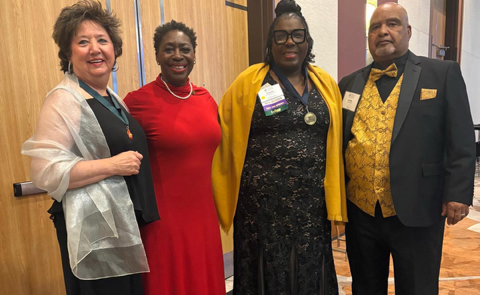 Four people stand together in evening attire inside a ballroom