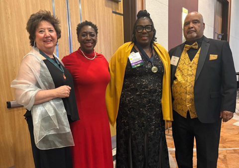 Four people stand together in evening attire inside a ballroom