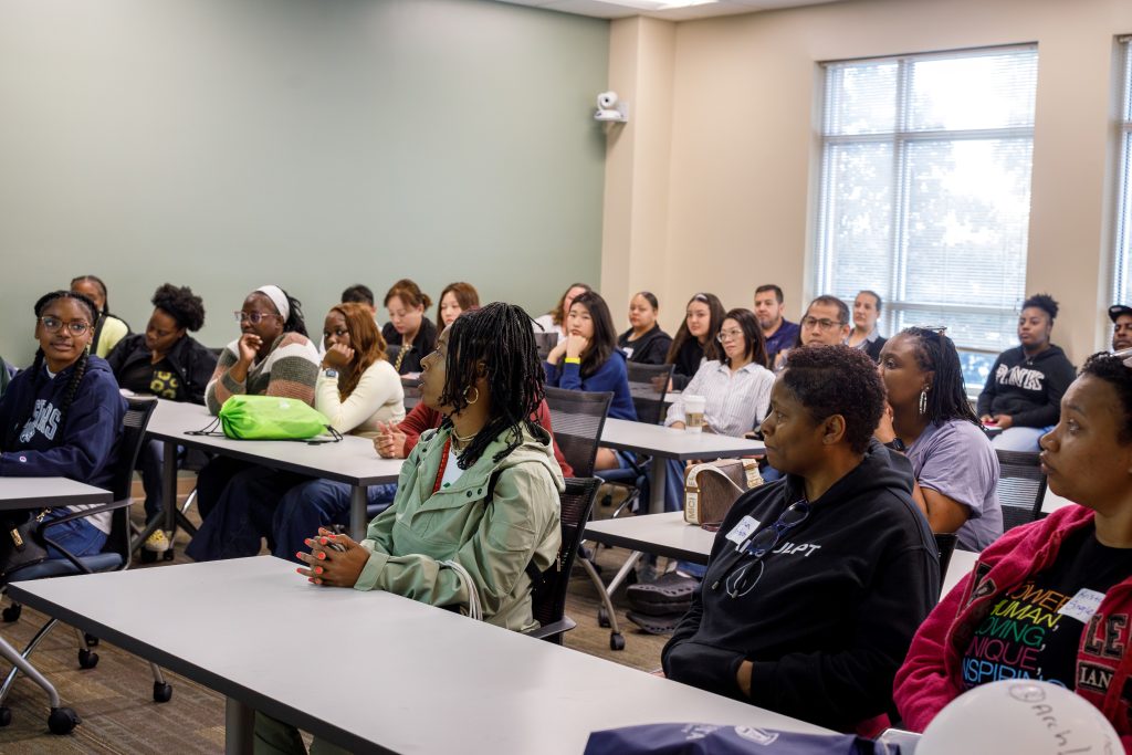 A group of men and woman sit inside a classroom.