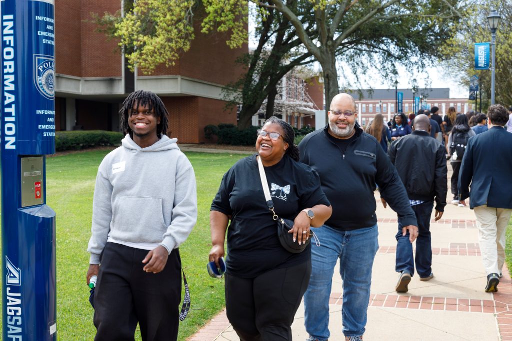 Two men and a woman walk down the sidewalk while smiling.