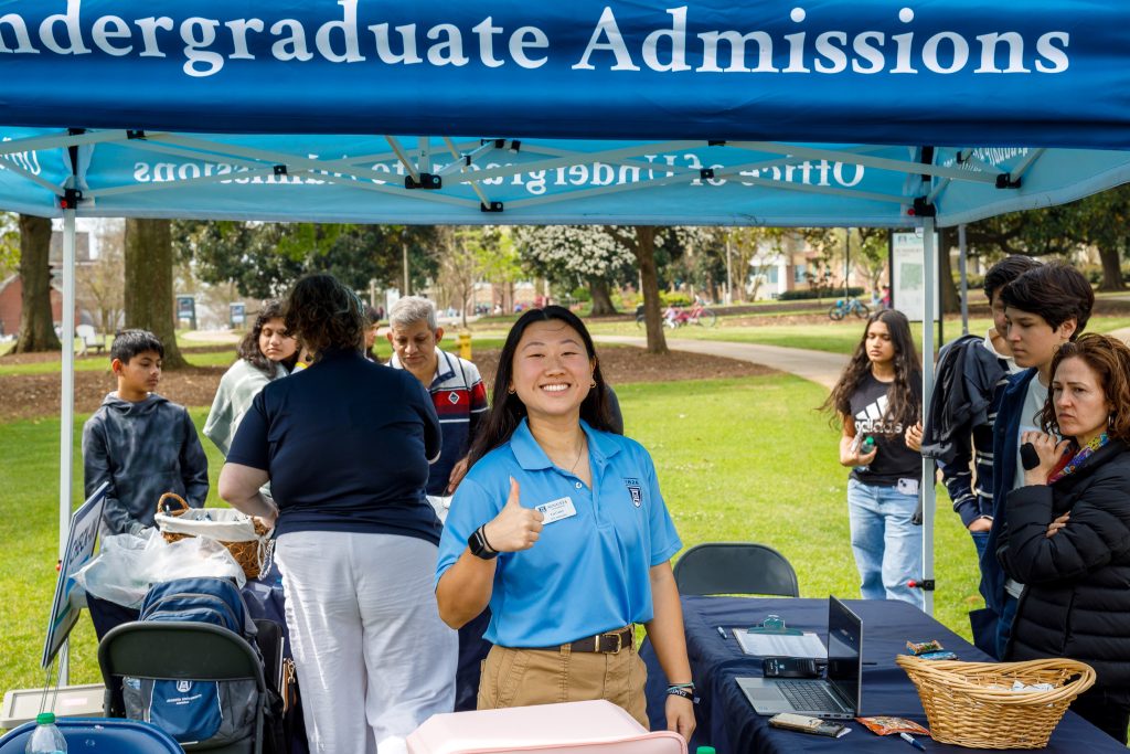 A woman stands underneath a table tent while holding a thumbs up.