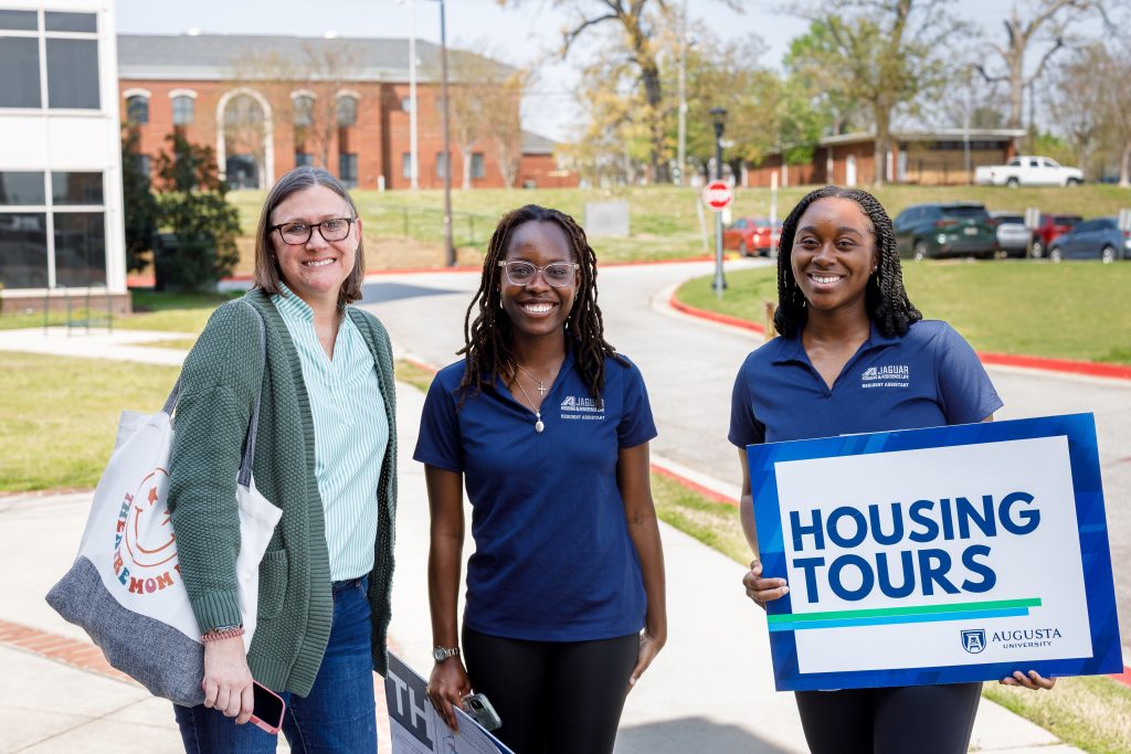 Three women are smiling, with one holding up a sign.