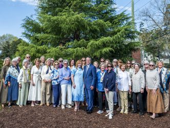 Large group of ladies and one man in front of a large tree.