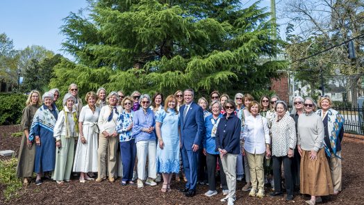 Large group of ladies and one man in front of a large tree.
