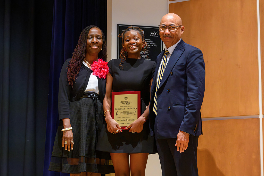 A woman and man standing with a student holding a plaque