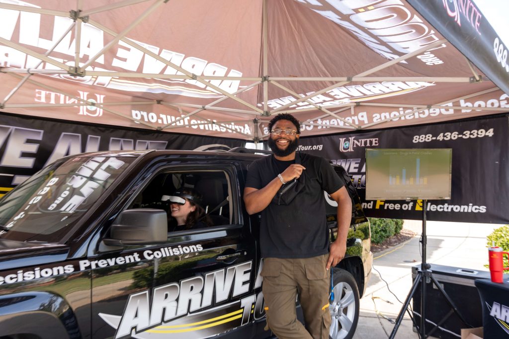 A woman wearing simulation googles sits in a vehicle while navigating an impact video.