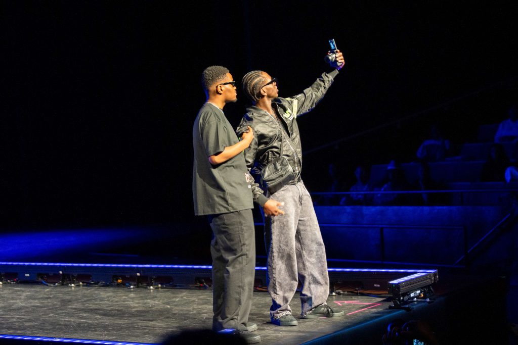 Two men pose for a selfie while at the end of a runway