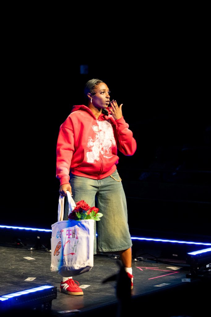 A woman at the end of a stage blows a kiss toward the audience. 