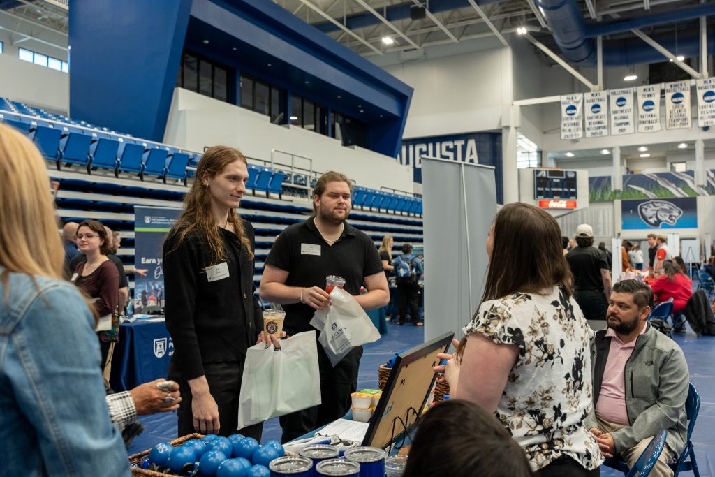 People stand talking at an indoor tabling event.