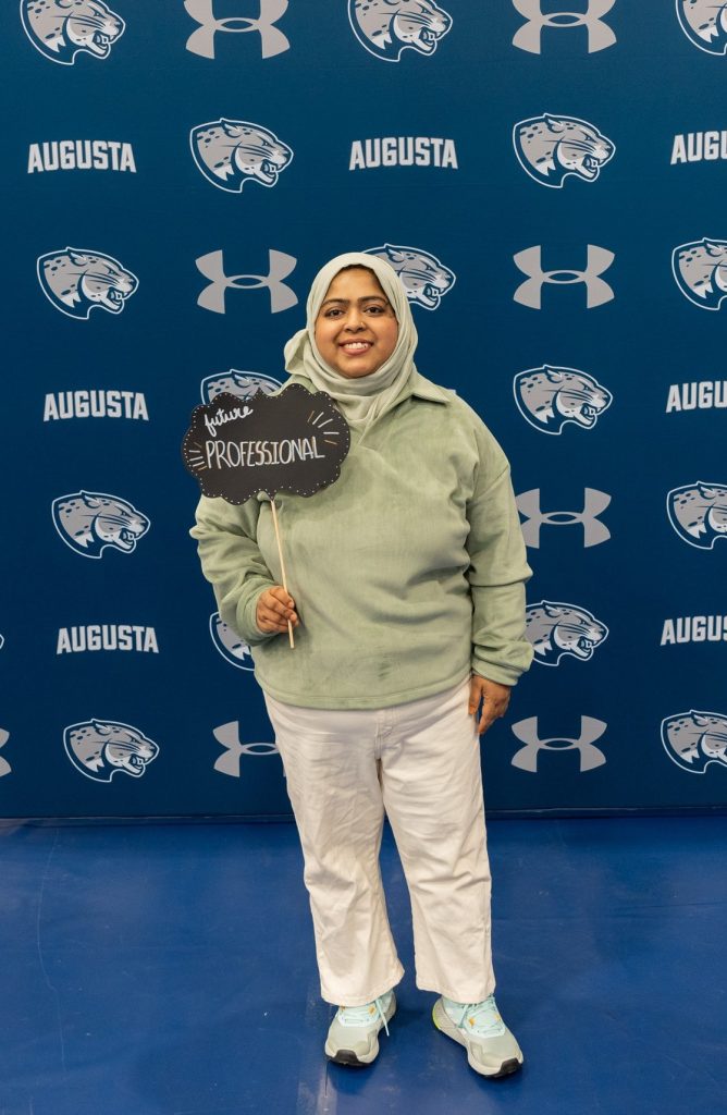 A girl poses for a photo while holding up a small future professional sign.