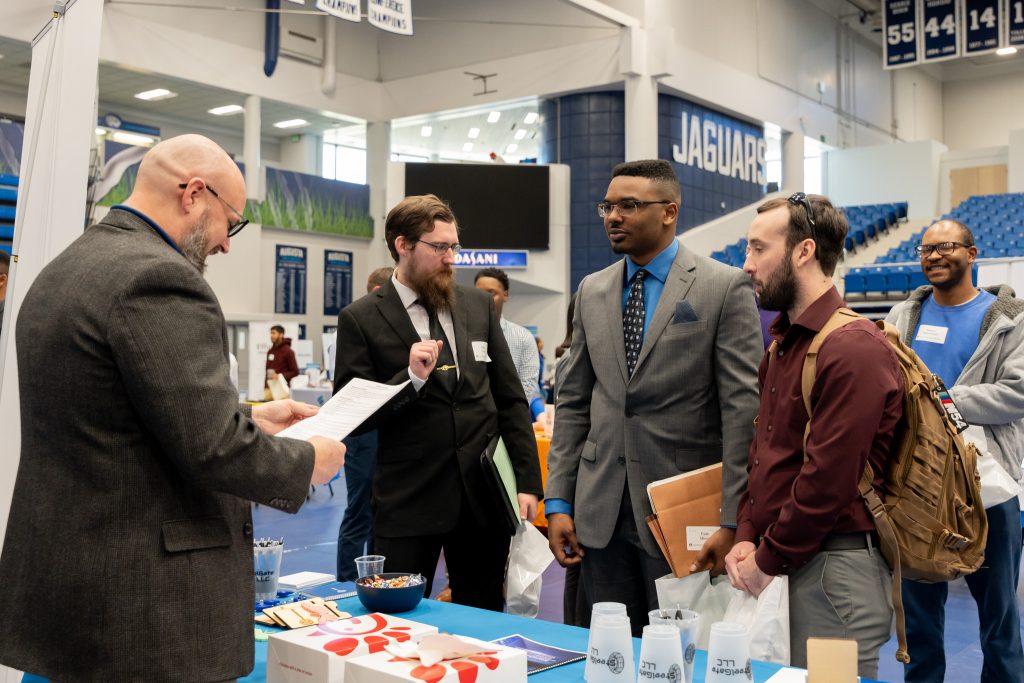 People stand talking at an indoor tabling event.
