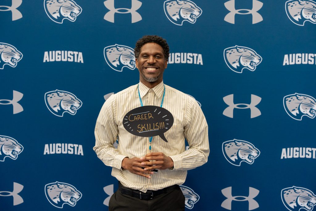 A smiling man poses for a photo while holding a small career skills sign.