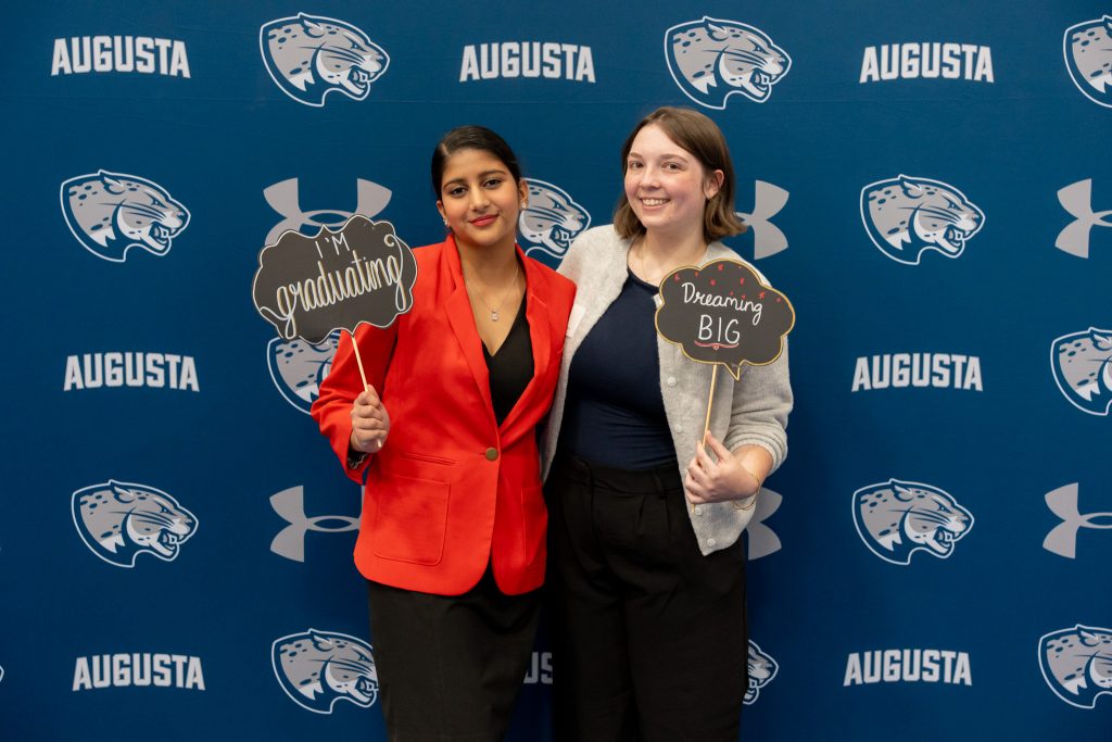 Two women smile for a photo while holding a soon-to-be graduating and dreaming big sign.