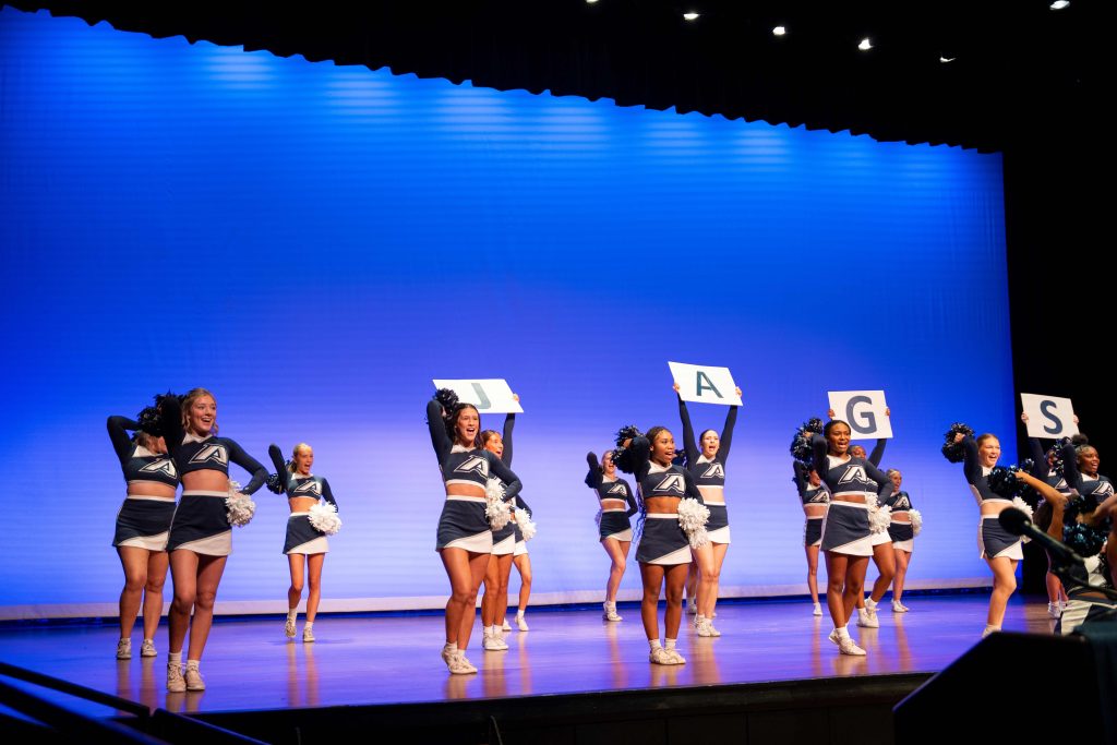 Cheerleaders hold up signs on a stage.
