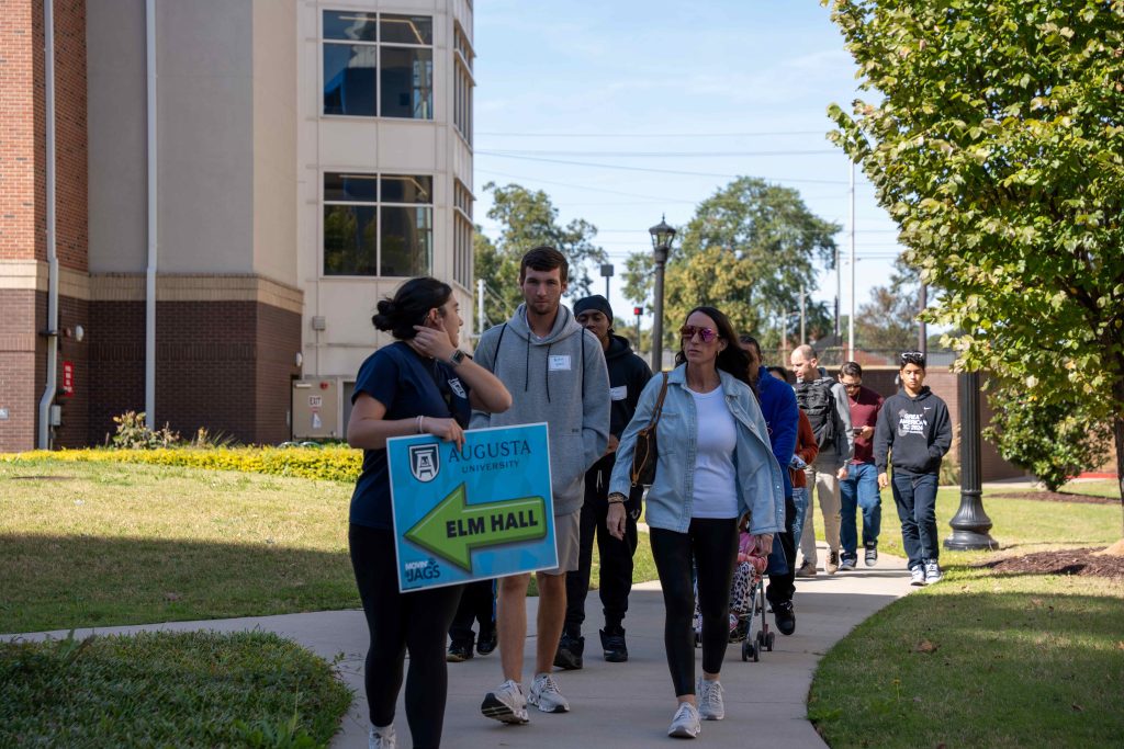 A young woman holds a sign while walking in front of a large group of people.