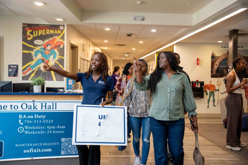 A young woman holds a sign while walking in front of a large group of people.