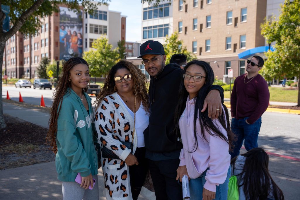 A family of four pose for a photo in front of the Augusta University residence halls.