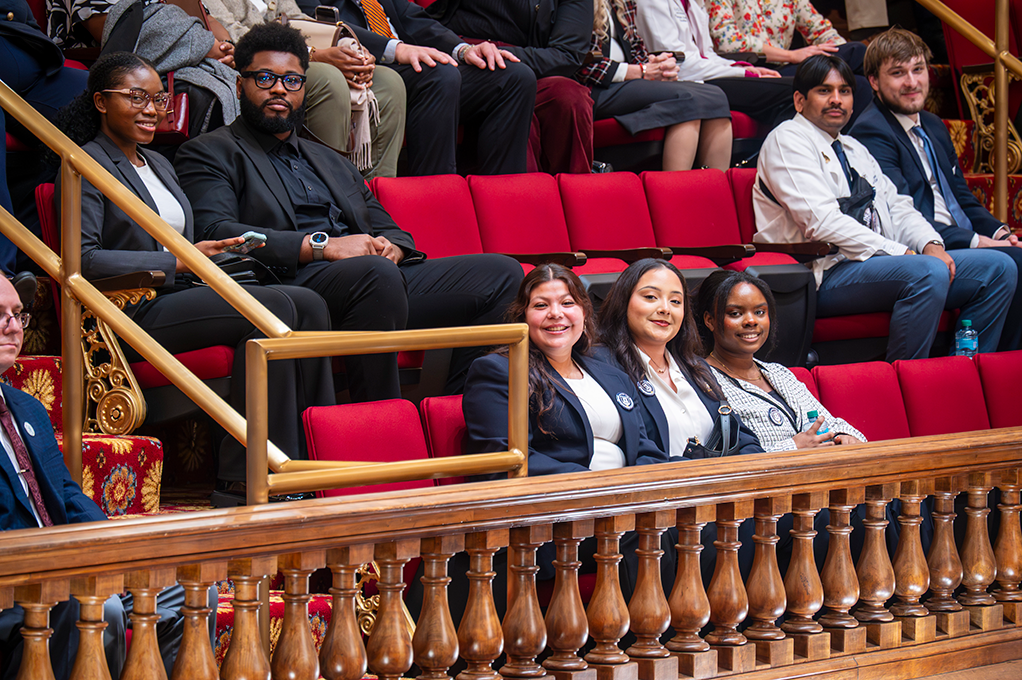 Young men and women sit in theatre type chairs in a gallery.