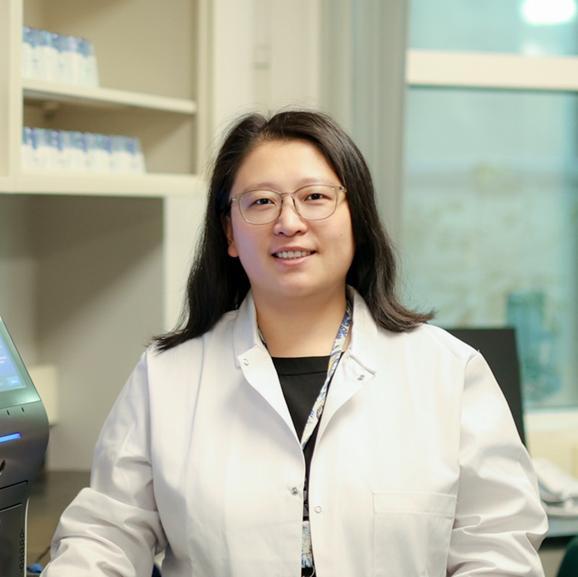 A female scientist wearing a lab coat smiles at the camera.
