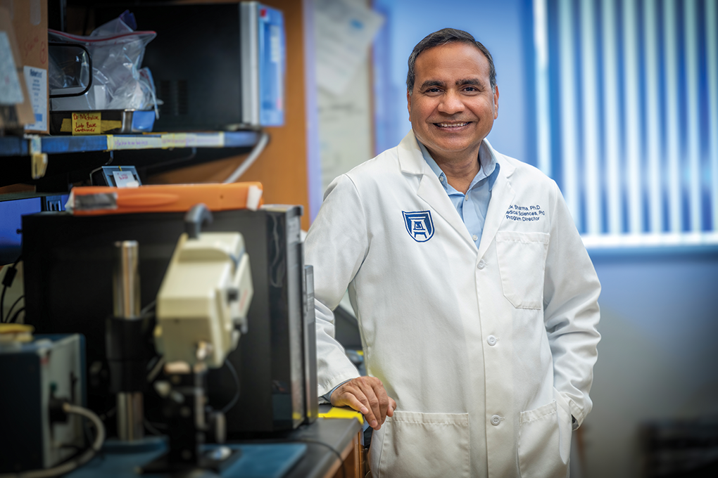 A male scientist stands in a lab and smiles at the camera.