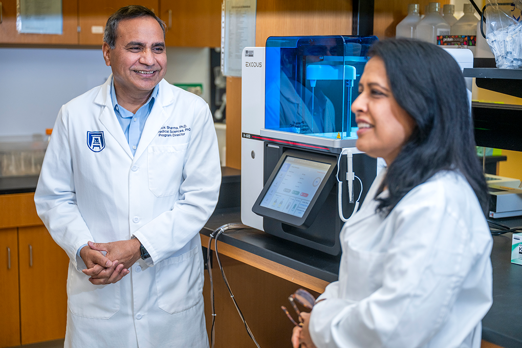 A male and female scientist wearing lab coats laugh in a lab.