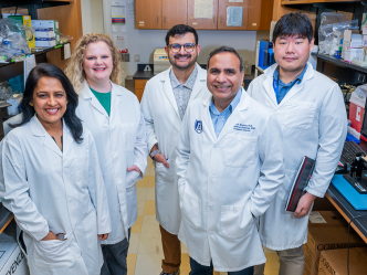 A group of male and female scientists wearing lab coats smile at the camera in a lab.