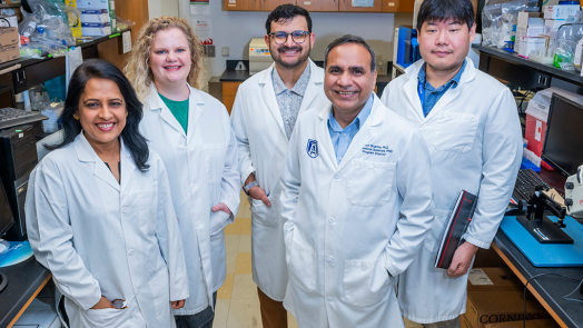 A group of male and female scientists wearing lab coats smile at the camera in a lab.