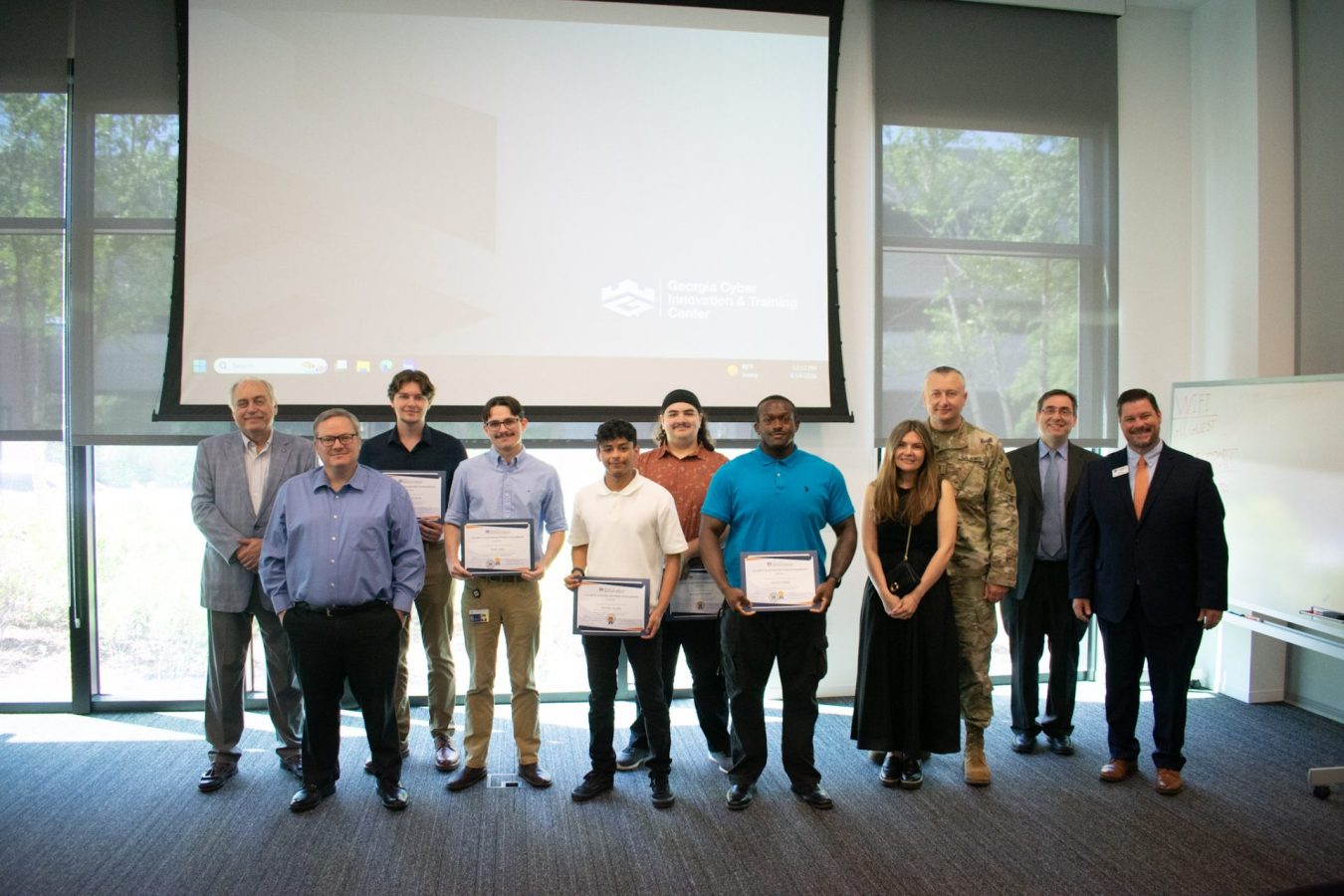 A group of men and one woman stand in front of a screen and hold awards.