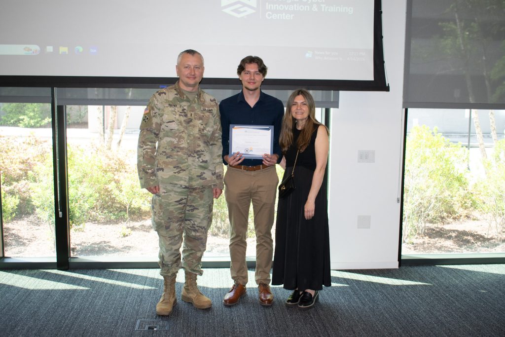 Two men standing with a woman with one man holding a certificate