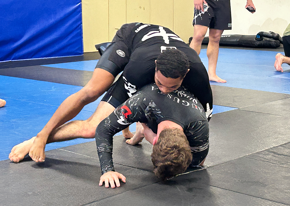 Two men Jiu-Jitsu spar on a mat.