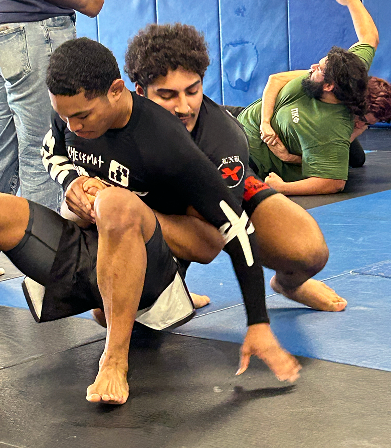 Two men Jiu-Jitsu spar on a mat.