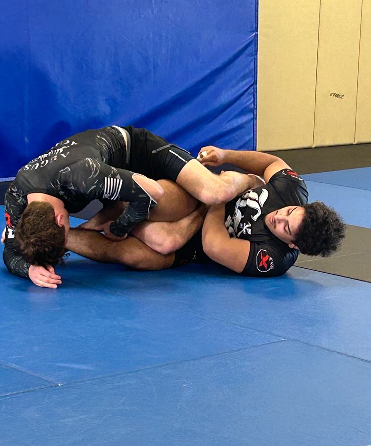 Two men Jiu-Jitsu spar on a mat.