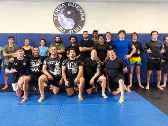 A group of men and woman wearing athletic gear pose for a group photo on a mat.