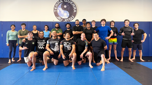 A group of men and woman wearing athletic gear pose for a group photo on a mat.