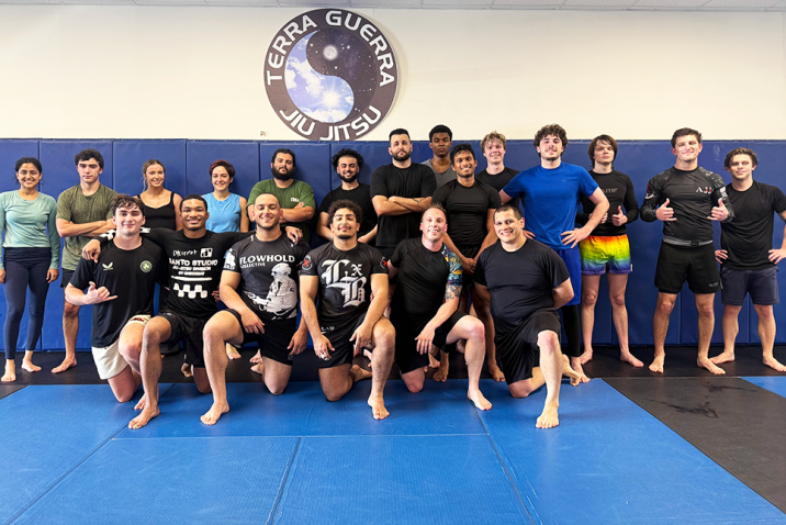 A group of men and woman wearing athletic gear pose for a group photo on a mat.