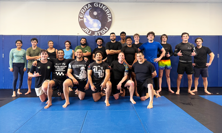 A group of men and woman wearing athletic gear pose for a group photo on a mat.
