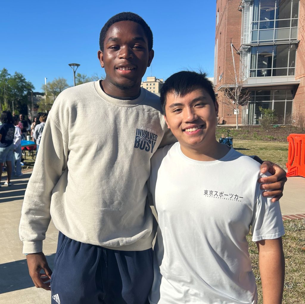 Two college-aged men with arms thrown around one another smile for a photo.