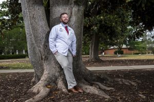 Man smiling leaning against a tree