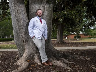 Man smiling leaning against a tree