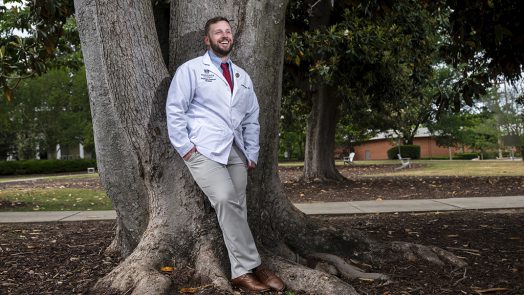 Man smiling leaning against a tree
