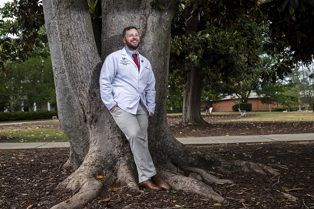 Man smiling leaning against a tree