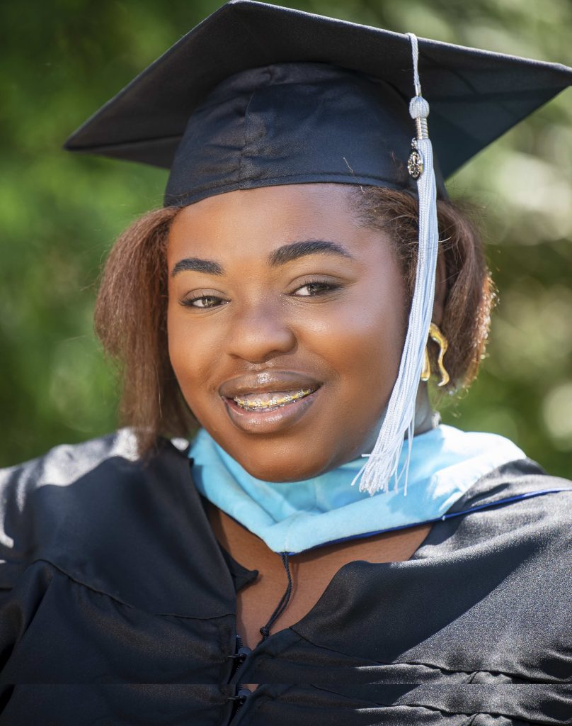 A woman wearing a graduate hood and gown smiles for a photo. 